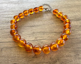 Betty chunky bead necklace with glossy amber brown acrylic beads and a silver-tone clasp on wood