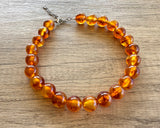 Betty chunky bead necklace with glossy amber brown acrylic beads and a silver-tone clasp on wood
