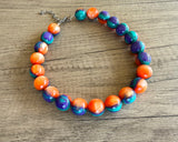 Betty chunky bead necklace with glossy orange, teal and purple acrylic beads and a silver-tone clasp on wood
