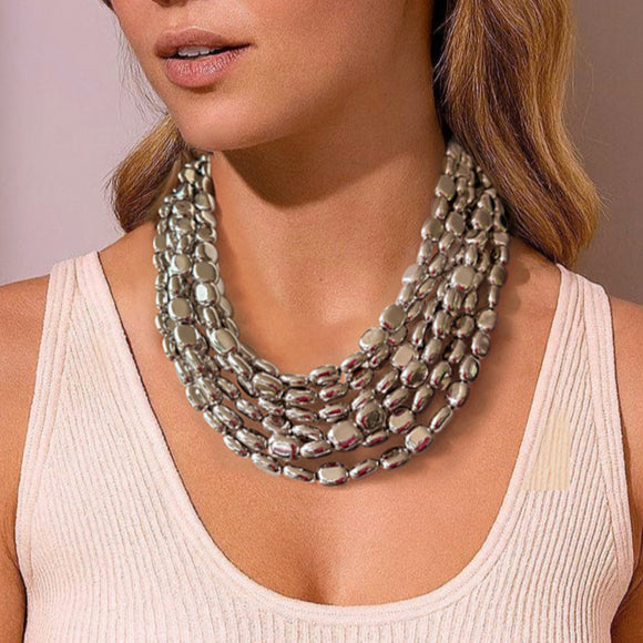 Woman wearing a shiny silver oval beaded multi strand necklace standing against a neutral background